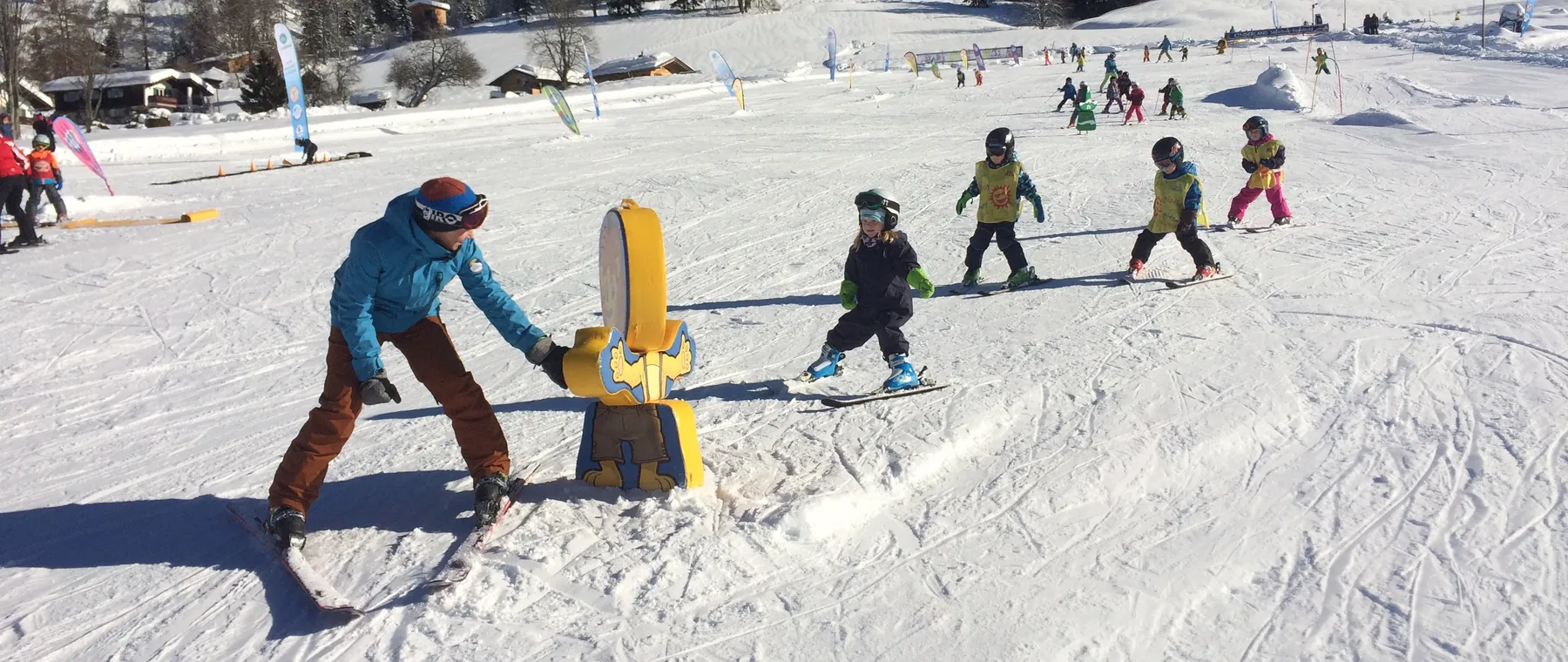 Skilehrer übt mit Kindern am Übungshang mit Figuren und Toren